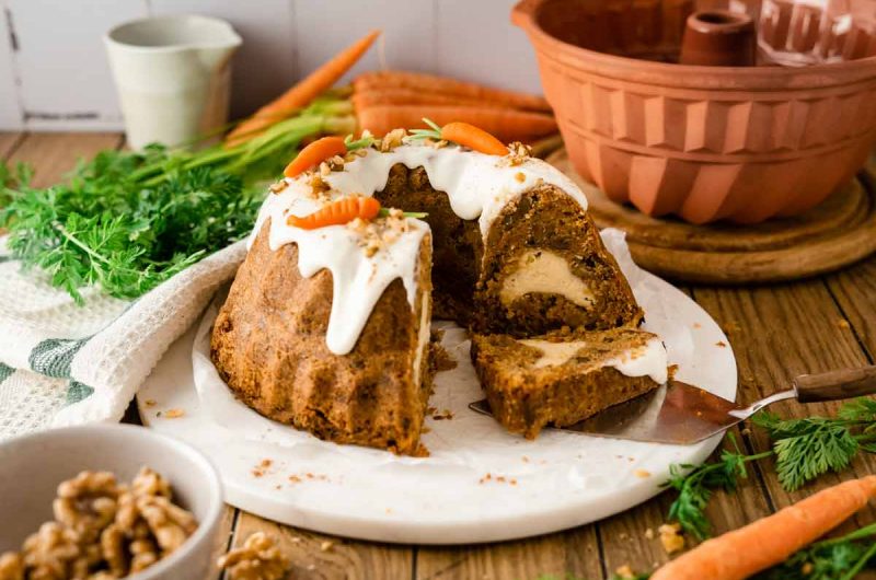 Karottenkuchen mit weißem Zuckerguss, garniert mit kleinen Marzipankarotten, serviert auf einem weißen Teller.