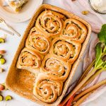 Frische Rhabarberschnecken in einer Backform, eine auf einem Teller serviert, mit frischem Rhabarber dekoriert.