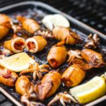 Gegrillte gefüllte Tintenfische auf einer Grillplatte mit Zitronenscheiben, angerichtet auf einem Grill.