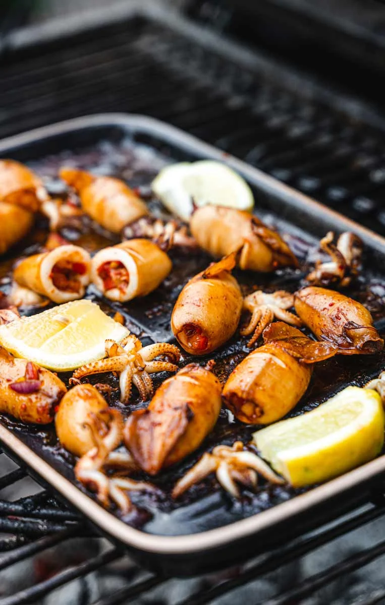 Gegrillte gefüllte Tintenfische auf einer Grillplatte mit Zitronenscheiben, angerichtet auf einem Grill.