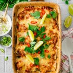 Ofenform mit überbackenen Enchiladas, garniert mit Limettenscheiben und Kräutern. Daneben Petersilie und saure Sahne.