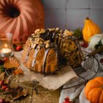 Kürbiskuchen mit Schokolade und Nüssen dekoriert auf einem Tisch mit Kürbissen und Herbstblättern.