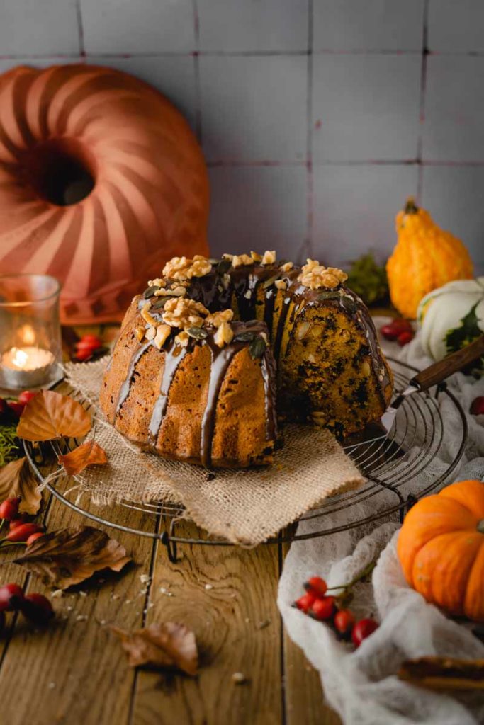 Kürbiskuchen mit Schokolade und Nüssen dekoriert auf einem Tisch mit Kürbissen und Herbstblättern.