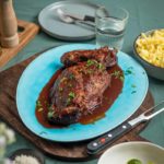 Geschmorte Entenkeule in Soße auf blauem Teller, mit Petersilie garniert. Beilage: Spätzle und Rosenkohl.