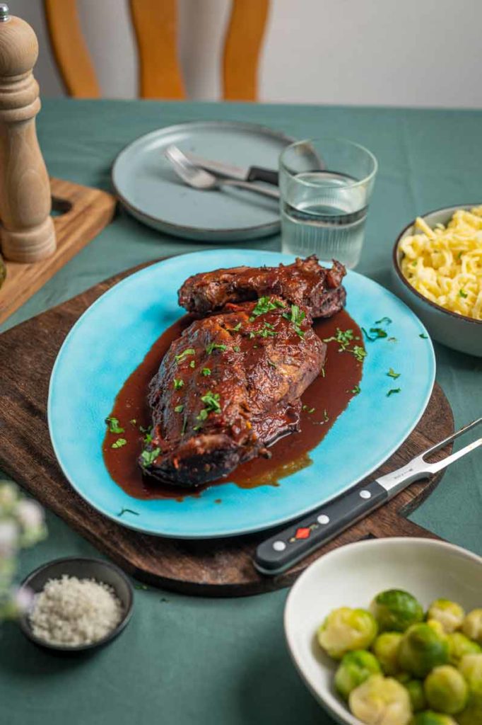 Geschmorte Entenkeule in Soße auf blauem Teller, mit Petersilie garniert. Beilage: Spätzle und Rosenkohl.