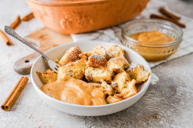 Schüssel mit Kaiserschmarrn und Apfelmus, dekoriert mit Puderzucker, auf einem Tisch mit Zimtstangen im Hintergrund.