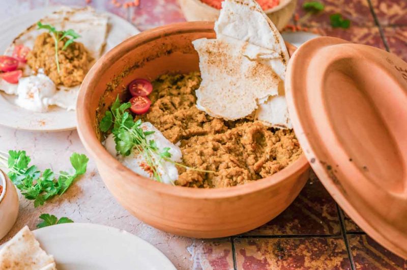 Ton-Schüssel mit Linsenpüree, garniert mit Tomaten, Joghurt, Kräutern und Fladenbrotstücke.