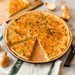 Zwiebelkuchen auf einem Teller mit einem angeschnittenen Stück, daneben ein Holzbrett mit einem weiteren Stück.