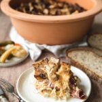 Ein Teller mit Sauerkraut, Fleisch und Brotstücken vor einem großen Tontopf und eingelegtem Gemüse.