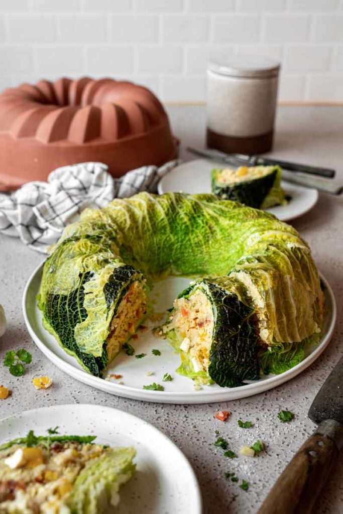 Kohlgugelhupf mit Füllung auf Teller, daneben Gugelhupfform und Besteck auf Küchentisch.