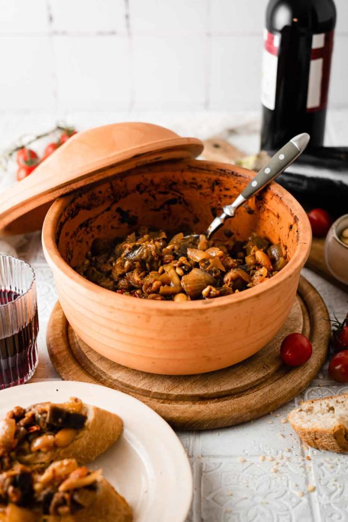 Terrakotta-Schüssel mit Bohneneintopf, daneben ein Glas Rotwein und Ciabatta-Scheiben auf einem Teller.