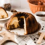 Anschnitt eines Gugelhupfs auf Teller, im Hintergrund Löffelbiskuits und Kaffeebohnen.