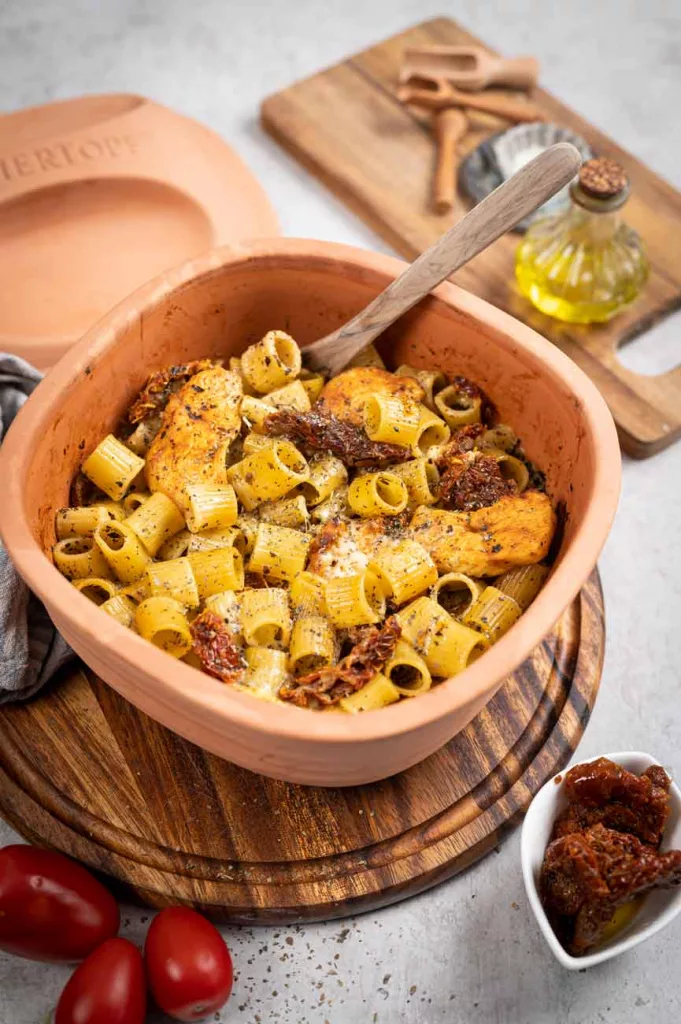 Tonform mit Pasta, Hähnchen und getrockneten Tomaten, daneben Gewürzöl und frische Tomaten.
