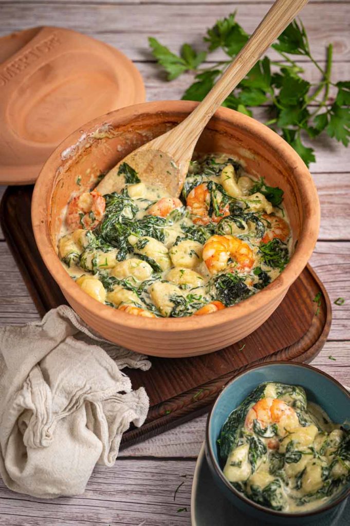 Ton-Topf mit Gnocchi, Spinat und Garnelen in cremiger Sauce, daneben eine Schüssel mit derselben Speise.