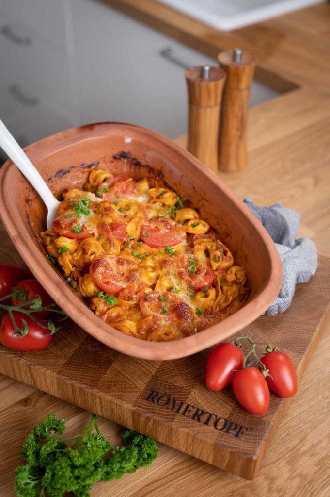 Gebratene Tortellini in Tomatensoße und Käse in einem Terrakotta-Behälter, dekoriert mit Petersilie.