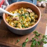 Schüssel mit Nudeln, Spinat, Thunfisch und Petersilie auf einem Holzbrett, daneben frische Kräuter.