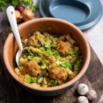 Keramikschale mit Nudeln, vegetarischen Bällchen und Kräutern auf Holztisch, daneben ein Römertopf-Deckel.