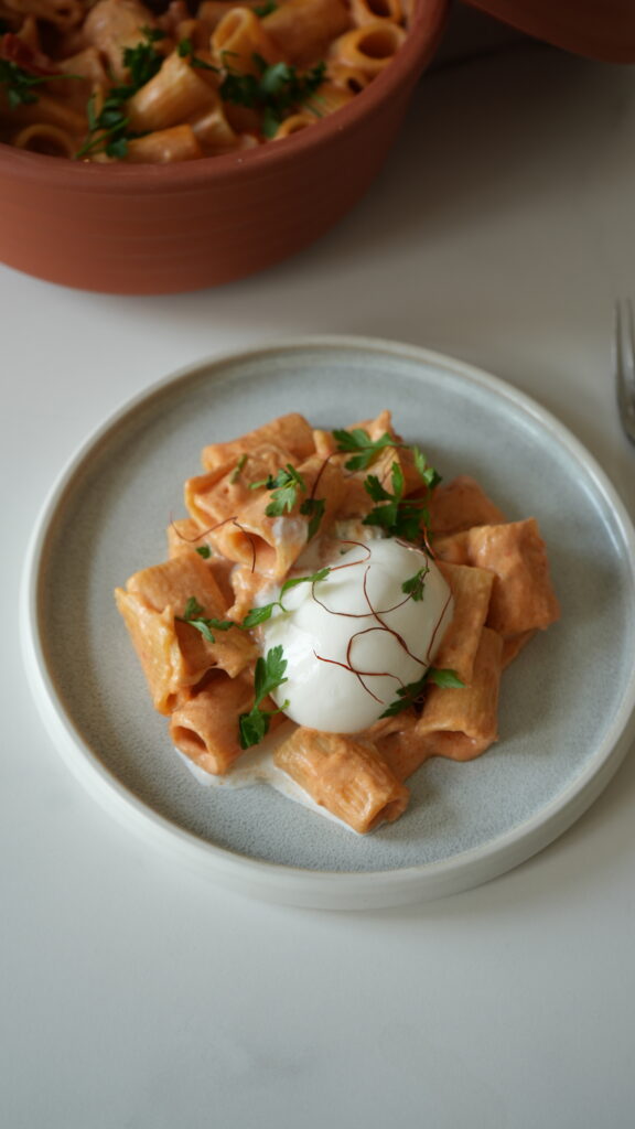 Rigatoni mit cremiger Sauce, garniert mit Petersilie und Safranfäden, serviert mit pochiertem Ei auf einem Teller.