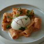 Rigatoni mit cremiger Sauce, garniert mit Petersilie und Safranfäden, serviert mit pochiertem Ei auf einem Teller.