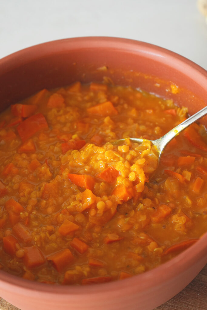 Rote Linsensuppe in einer Schüssel mit einem silbernen Löffel, auf dem ein Servierlöffel Suppeneintopf liegt.