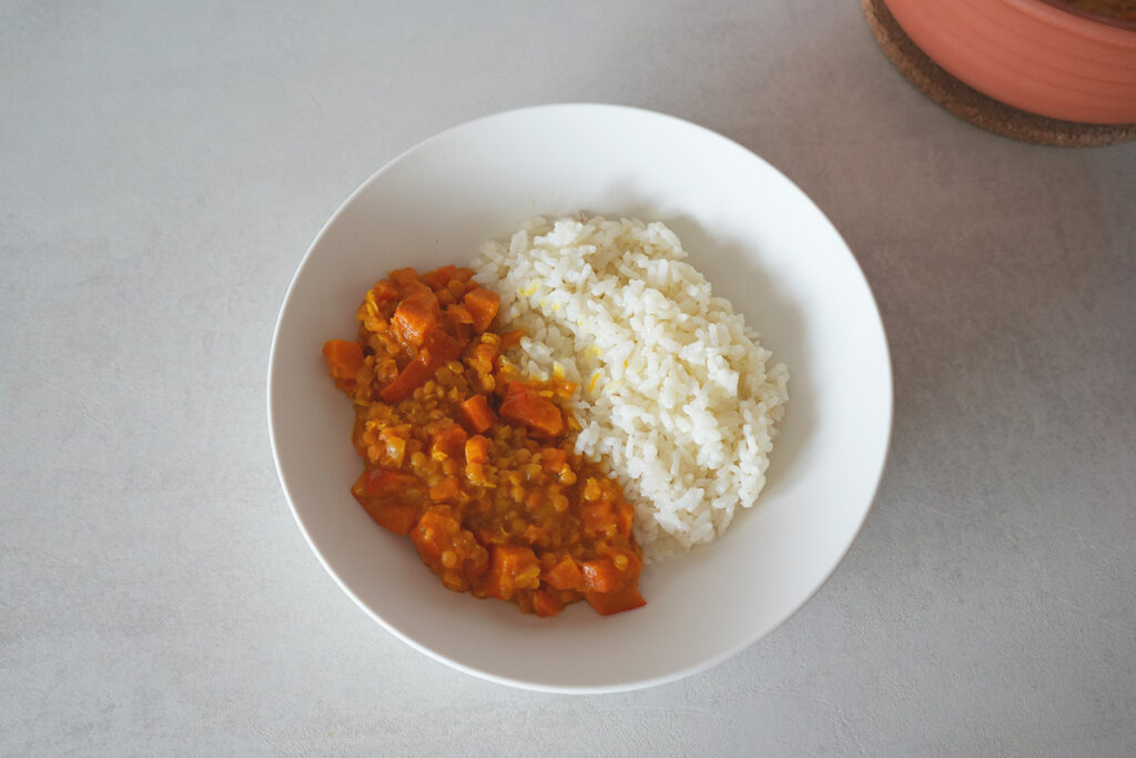 Rote Linsensuppe in einer Schüssel mit einem silbernen Löffel, auf dem ein Servierlöffel Suppeneintopf liegt.
