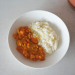 Rote Linsensuppe in einer Schüssel mit einem silbernen Löffel, auf dem ein Servierlöffel Suppeneintopf liegt.