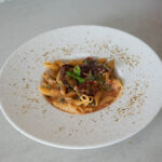 Teller mit cremiger Penne in Tomatensauce, garniert mit getrockneten Tomaten, Basilikum und Kräutern.