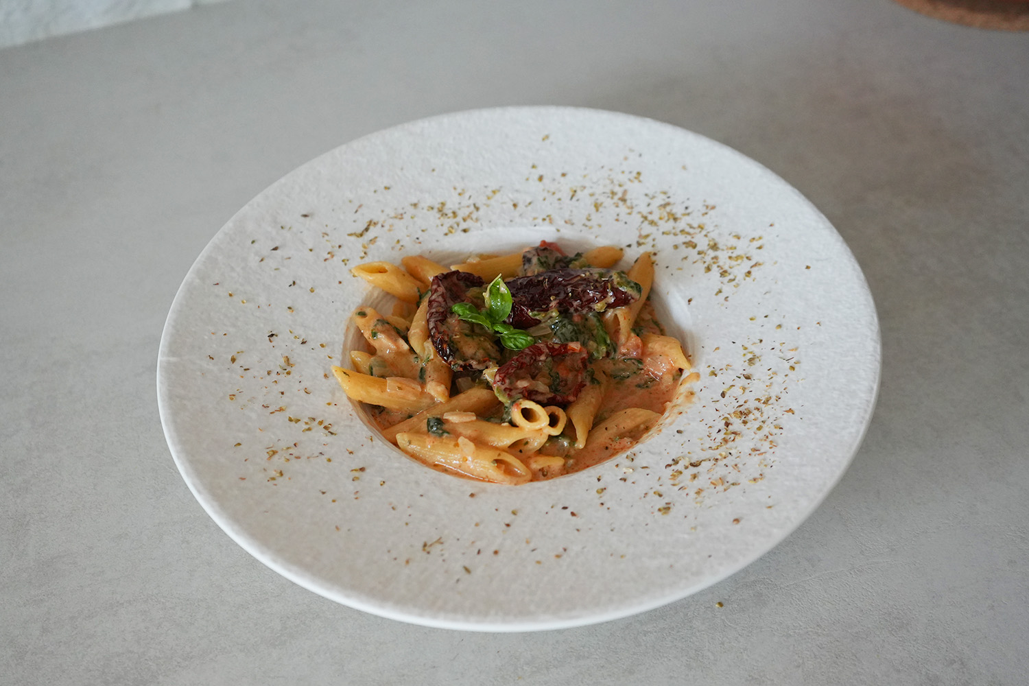 Teller mit cremiger Penne in Tomatensauce, garniert mit getrockneten Tomaten, Basilikum und Kräutern.
