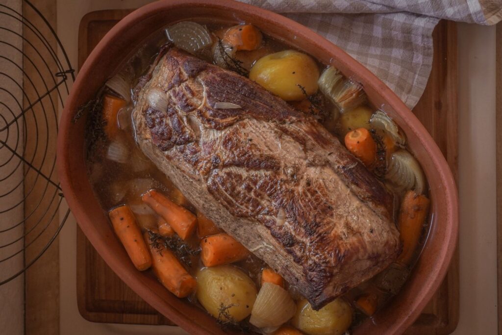 Braten im Schmortopf mit Kartoffeln, Karotten und Zwiebeln auf einem Holzbrett, bereit zum Servieren.