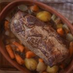 Braten im Schmortopf mit Kartoffeln, Karotten und Zwiebeln auf einem Holzbrett, bereit zum Servieren.