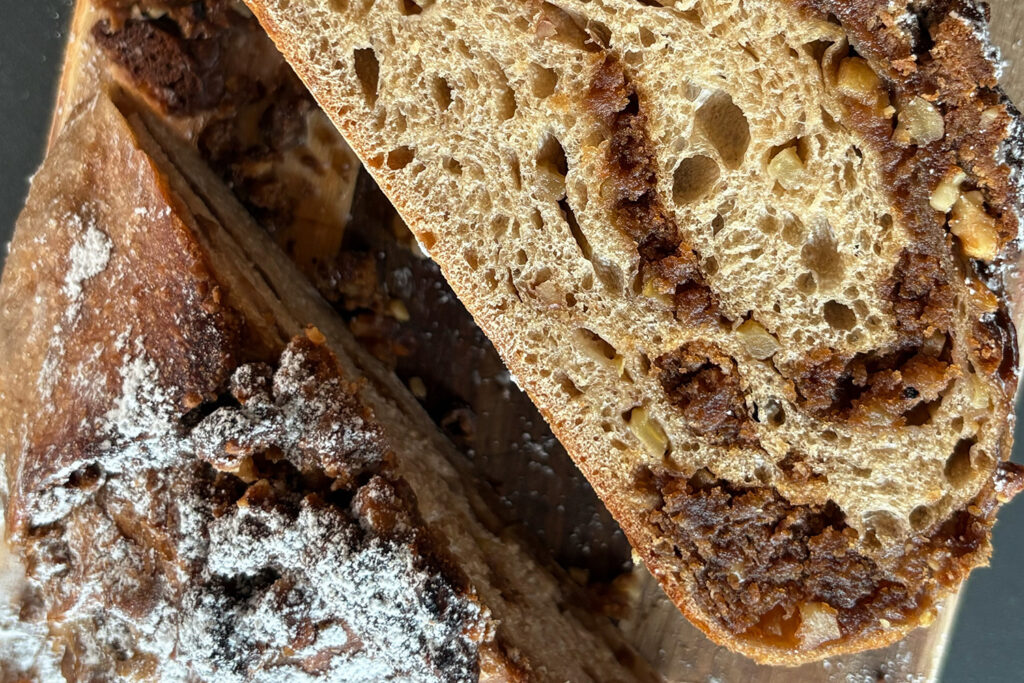 Nahaufnahme von zwei Scheiben Nussbrot mit Rosinen, außen mit Puderzucker bestreut.