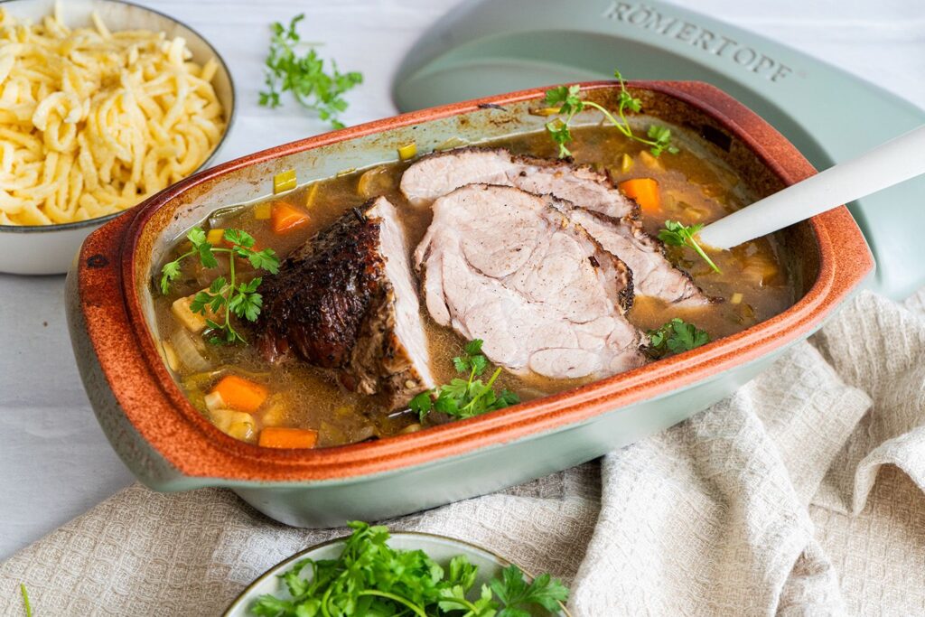 Saftiger Schweinebraten im Römertopf Culinario, angeschnitten mit aromatischer Sauce und frischer Petersilie, dazu Spätzle