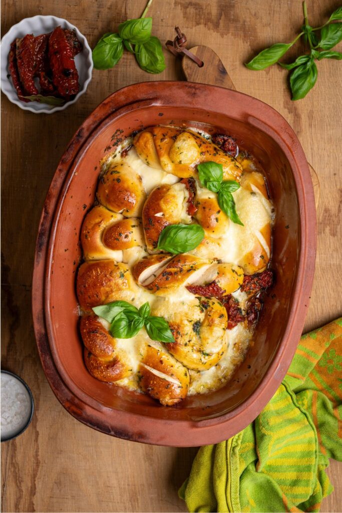 Goldbraun gebackenes Laugen Grillbrot mit Kräuteröl, Mozzarella und Tomaten von oben im Tontopf auf Holzbrett