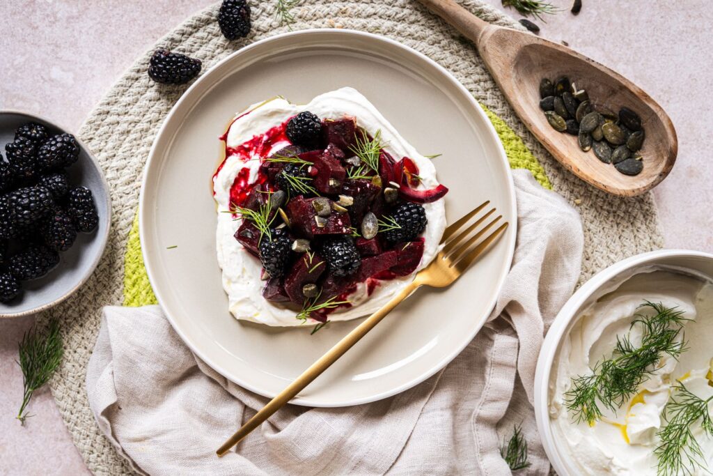 Gebackene Rote Bete mit cremigem Labneh, frischen Brombeeren, Kürbiskernen und Dill auf weißem Teller von oben