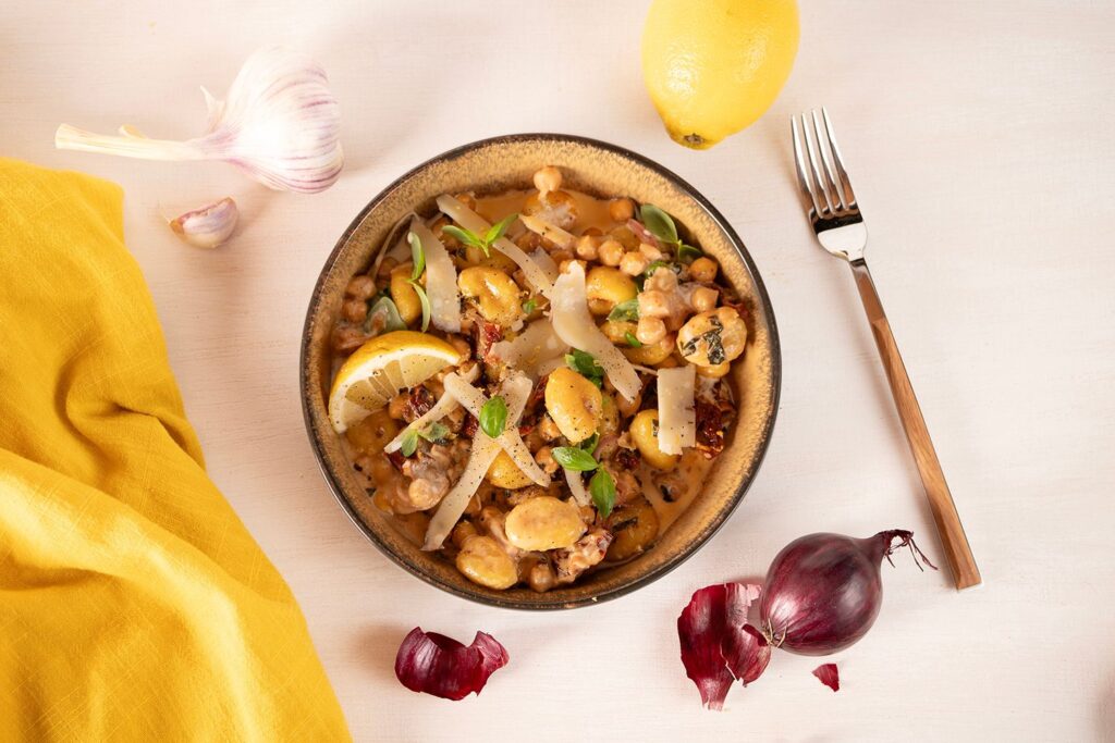 Gnocchi mit Kichererbsen in cremiger Tomatensauce mit Parmesan, Basilikum und Zitrone in einem dunklen Schälchen von oben