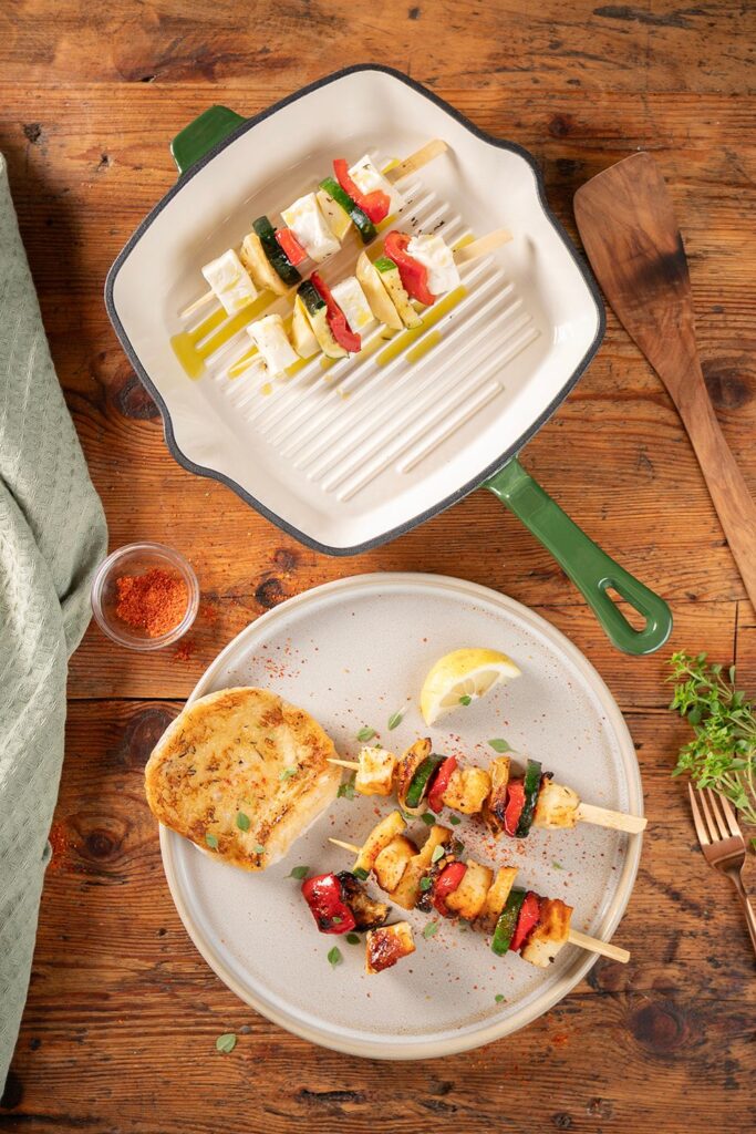 Halloumi Gemüsespieße vor und nach dem Grillen in der grünen gusseisernen Grillpfanne, dazu geröstetes Weißbrot und Zitronen auf einem Teller von Moritz und Moritz