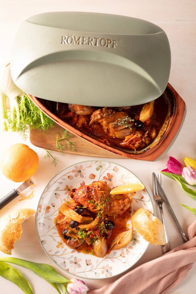 Geschmortes Kaninchen mit Fenchel und Orangen im geöffneten Römertopf Classico Bräter, daneben eine Portion auf einem geblümten Teller angerichtet