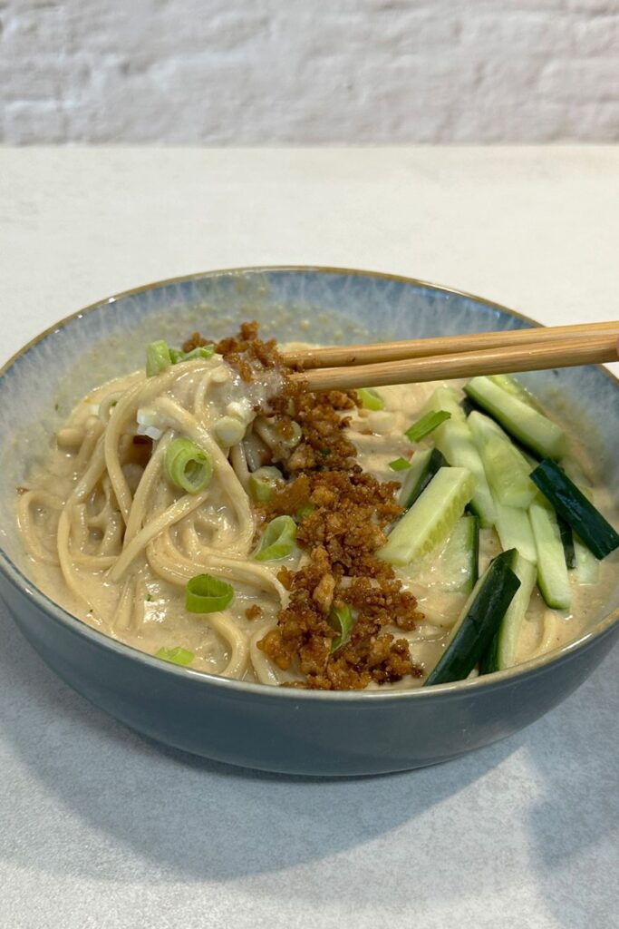 Ramen Bowl mit Crispy Tofu und Nudeln in Kokosbrühe, mit Stäbchen beim Servieren – Nahaufnahme