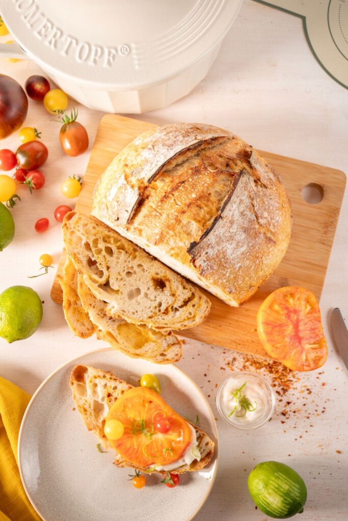 Angeschnittenes Chakalaka Sauerteigbrot mit Tomaten belegt auf Teller, daneben Aioli-Dip und frische Limetten