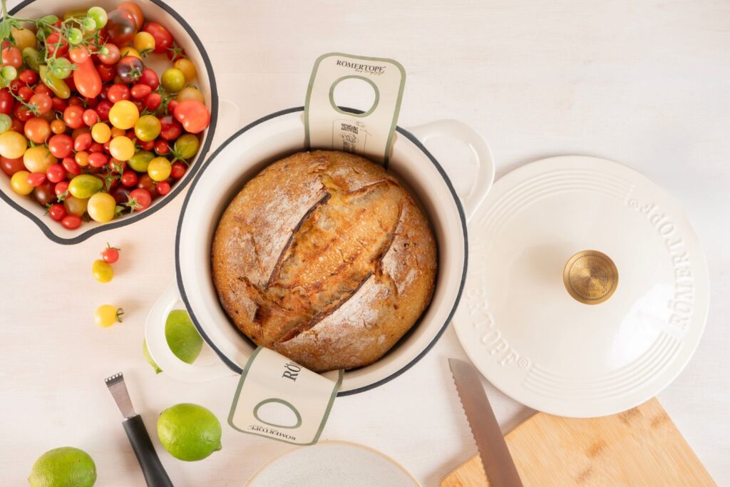 Chakalaka Sauerteigbrot im weißen gusseisernen Topf von oben, umgeben von bunten Tomaten und Limetten