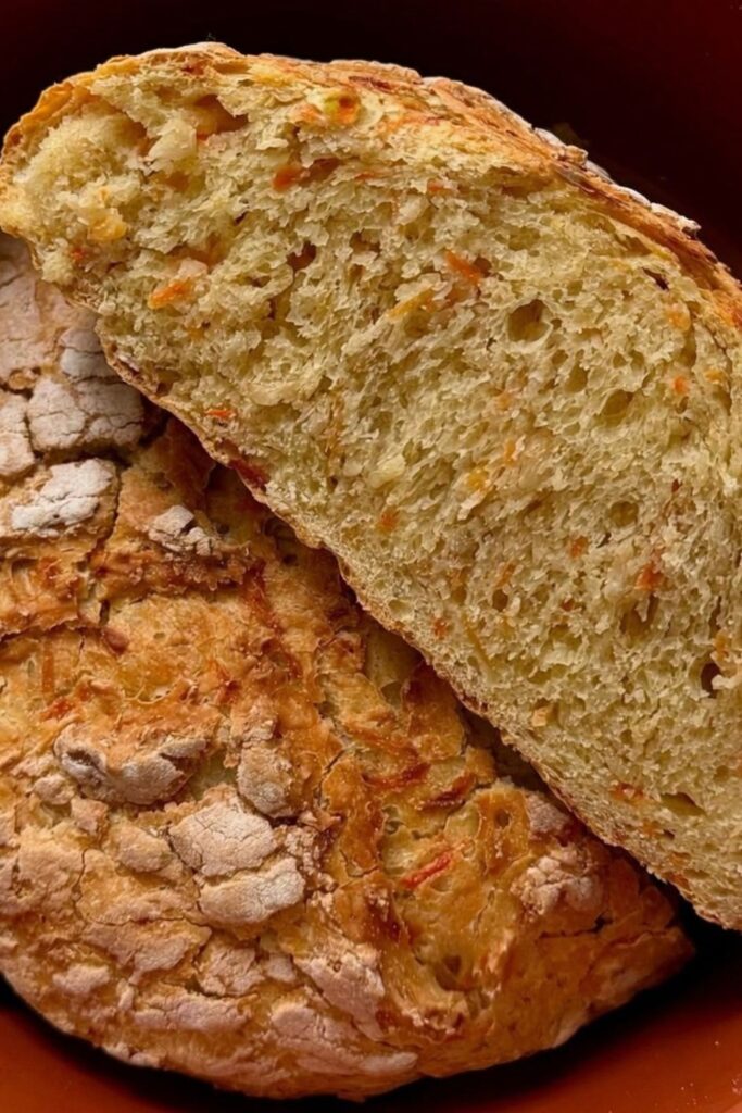 Aufgeschnittenes Karotten-Dinkelbrot mit sichtbaren Karottenstückchen in der Krume, im Hintergrund dunkler Topf