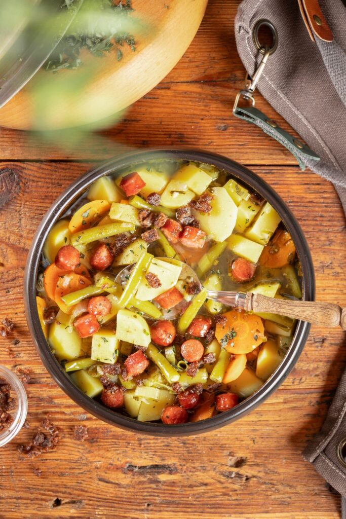 Nahaufnahme der Kartoffelsuppe mit Würstchen und Pumpernickelcrunch, Löffel im Topf