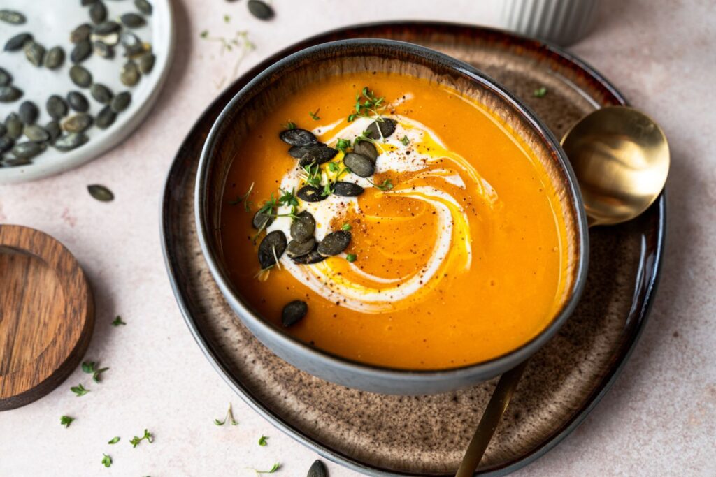 Klassische Kürbissuppe mit Crème-fraîche-Wirbel, Kresse und Kürbiskernen in dunkler Schale