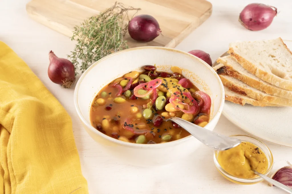 Bunte vegane Bohnensuppe mit Edamame, Kidneybohnen und pinken Limettenzwiebeln in einer Schale