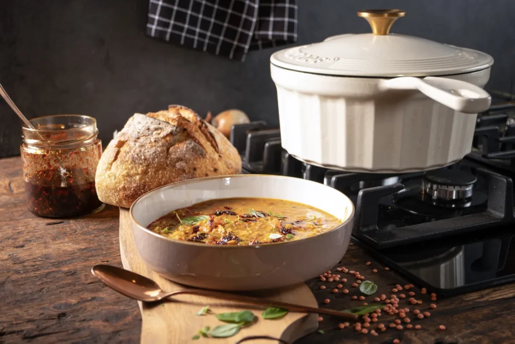 Glas mit selbstgemachtem Crispy Chili Oil neben einer Schale Linsensuppe