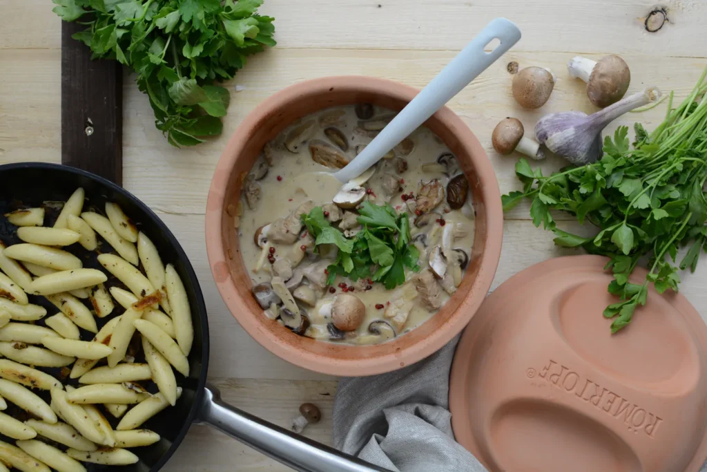 Filettopf mit Champignons und Rahmsoße im Römertopf, daneben Schupfnudeln in der Pfanne