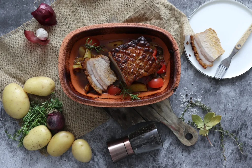 Schweinebauch mit knuspriger Kruste auf Kartoffeln, Paprika und Tomaten im Römertopf